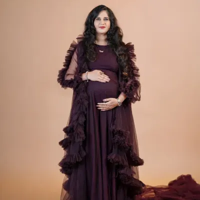 A full-length portrait showcasing a dramatic, dark purple ruffled maternity gown against a neutral studio backdrop. This look is perfect for creating an elegant and high-fashion feel for your pregnancy photos.