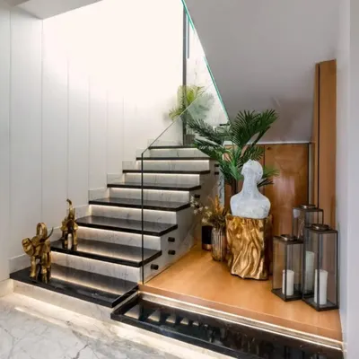 This stunning staircase in our Santacruz project features black marble steps with integrated lighting and a glass railing. The surrounding decor creates a grand and elegant entryway.