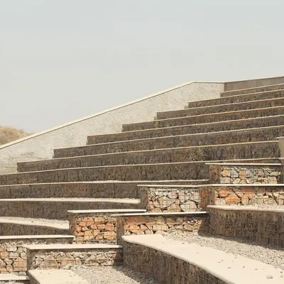The stepped seating of the Aravali Biodiversity Park Amphitheatre is constructed with gabion walls, which are wire mesh cages filled with stones sourced directly from the site. This sustainable technique minimizes waste and ensures the structure is visually integrated with the landscape.