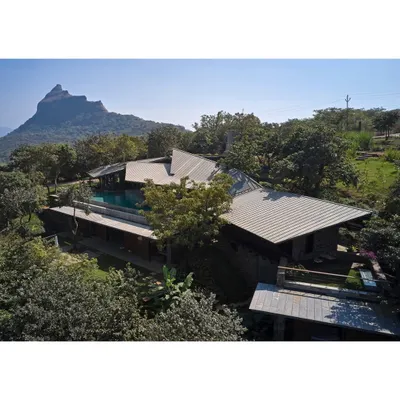 An elevated view of the Lateral Verandah House, nestled within the lush landscape of Lonavala. The structure's fragmented form is a deliberate strategy to minimize its impact on the site and maximize its engagement with the natural environment and distant views.