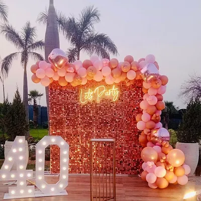A chic outdoor 40th birthday celebration. This setup features a rose gold sequin wall, a "Let's Party" neon sign, and large marquee numbers on a wooden deck, perfect for an evening party.