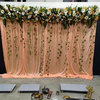 A simple and elegant backdrop for a 25th-anniversary celebration, featuring a peach-colored curtain, a floral topiary, and hanging green vines.