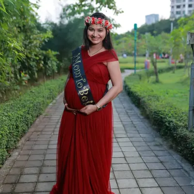 A happy mom-to-be in a simple yet elegant red maternity gown, perfect for an outdoor photoshoot. The empire waistline and soft tulle are designed for a comfortable fit while looking beautiful.