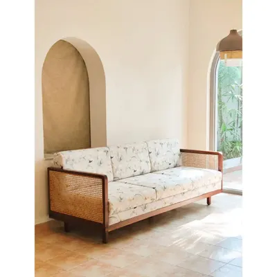 The Gubbi Sofa, a perfect blend of solid teak wood, natural rattan, and customizable floral fabric. Its clean lines and natural materials make it a versatile and elegant centerpiece for any living room.