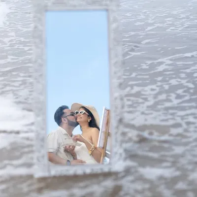 A creative and romantic kiss reflected in a mirror placed on the beach. This artistic shot from a Goa pre-wedding shoot is unique and memorable.
