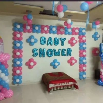 A classic baby shower decoration in a home setting. This setup uses a combination of pink, blue, and white balloons to create a festive wall backdrop, with large foil letters spelling out 'BABY SHOWER' as the main focus.