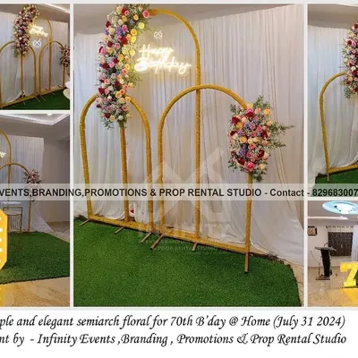 A simple and elegant floral setup for a 70th birthday celebration at home. The decor features golden semi-arches adorned with beautiful flowers and a "Happy Birthday" neon sign.
