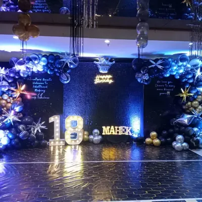 A grand and glamorous 18th birthday setup. The decoration features a dark, starry theme with a large dance floor, marquee numbers, and a balloon arch in shades of blue, black, and silver.