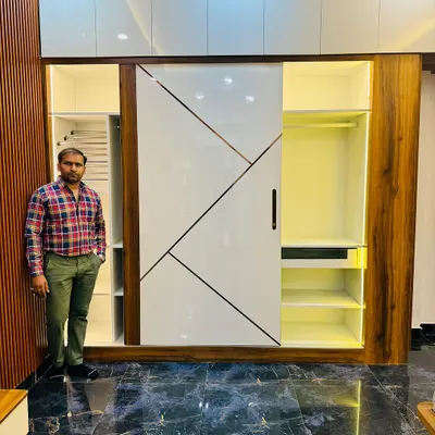 This is a floor-to-ceiling sliding wardrobe with a modern geometric design on the shutters. The combination of high-gloss white and wood finish gives the room a spacious and elegant feel.