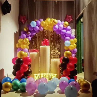 The space is all set for a kitty party. This colorful setup with a multi-colored balloon arch and "KITTY" spelled out in letters creates a fun and welcoming vibe for your group.