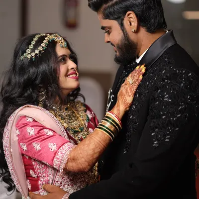 A sweet, romantic moment between the couple. The bride's makeup is soft and glowing, perfect for an engagement ceremony, complementing her pink lehenga beautifully.