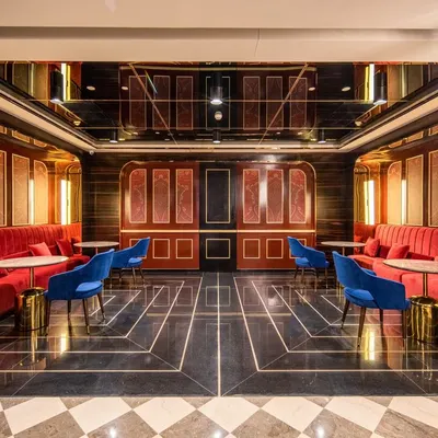 This private lounge area at INOX, Rajouri Garden, offers a luxurious pre-movie experience. The design uses rich red velvets, dark wood paneling, and a reflective ceiling to create an intimate and opulent atmosphere, reminiscent of classic Hollywood glamour.