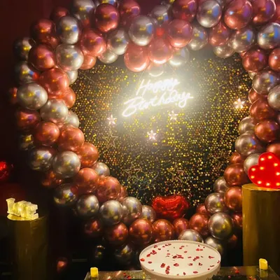 A classic birthday setup featuring a heart-shaped arch with red and silver chrome balloons, a 'Happy Birthday' neon sign, and a cake stand ready for the main event. This is one of my most requested romantic birthday themes.