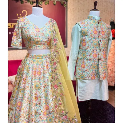 A front view of our festive couple set, displayed on mannequins to show the complete look. The woman's lehenga is paired with a matching embroidered blouse and a yellow dupatta, while the man's outfit features a Nehru jacket over a mint-green kurta.