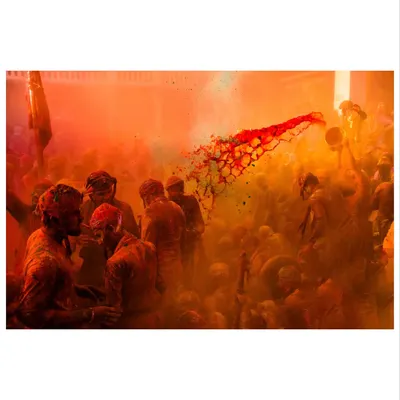 A jet of red color explodes through a cloud of orange powder during Holi. Capturing these split-second moments of action is what makes festival photojournalism so thrilling.