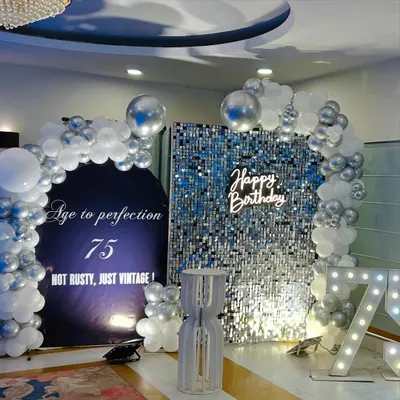 A sophisticated 75th birthday setup featuring a silver shimmer wall paired with a white "Happy Birthday" neon sign. The combination creates a modern and elegant look.