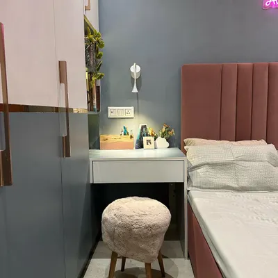 This guest room corner shows a compact and functional design. A small vanity desk is neatly tucked beside the bed, paired with a textured stool. The two-tone wardrobe with rose gold handles adds a touch of modern elegance, while the playful wall paint detail brings character to the space.