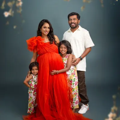 A beautiful family portrait celebrating their growing family. The mother's vibrant red gown stands out against the classic studio backdrop, while her two daughters lovingly embrace her baby bump.