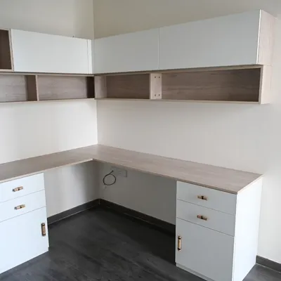 An L-shaped study workstation designed to comfortably accommodate two people. This functional desk includes ample drawer storage, overhead cabinets for books and files, and is finished in durable wood and matt laminates with elegant metallic antique handles.