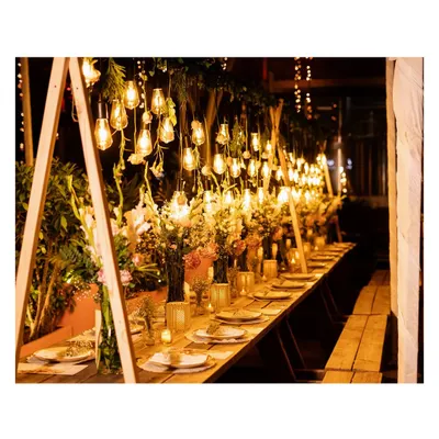 The full view of our "Blooms & Barrels" anniversary dinner setup. The combination of rustic wooden tables, hanging lights, and abundant fresh flowers creates a warm and inviting atmosphere for a memorable evening.