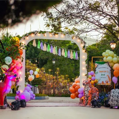 A grand entrance arch welcomes guests to Saachi's 2nd birthday, featuring life-sized animal props, lush greenery, and warm lighting for a magical evening safari.