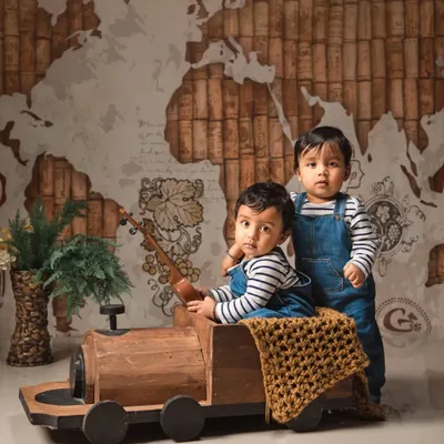 Twin boys ready for a journey in this travel-themed setup. The world map backdrop and wooden train prop create a sense of adventure for their combined photoshoot.