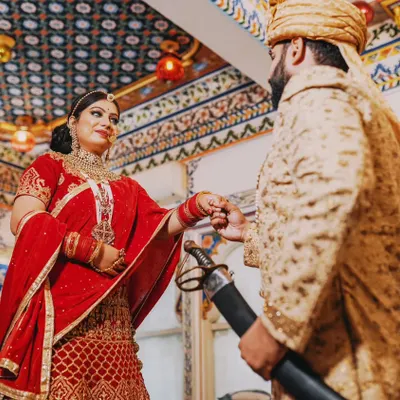 A moment of royal connection inside a beautifully ornate Udaipur palace. The groom, dressed in a classic sherwani, gently holds his bride's hand, showcasing the elegance and heritage of a Rajasthani theme.