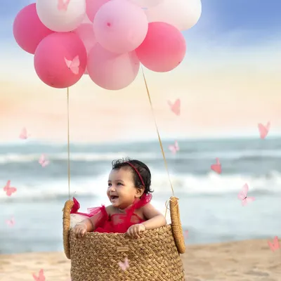 Let your dreams take flight. This creative beach photoshoot uses a "hot air balloon" prop made of a basket and pink balloons to create a whimsical, magical portrait against the ocean backdrop.