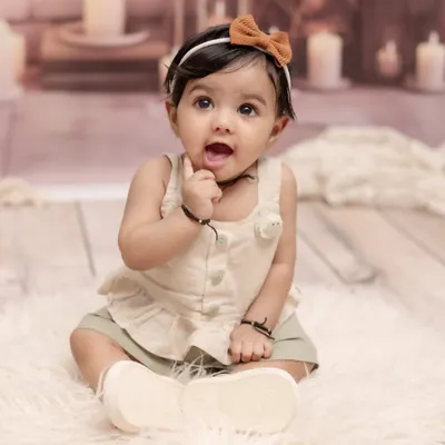 Capturing that curious and adorable sitter stage. This simple and sweet portrait of a baby girl, sitting up and exploring, focuses on her bright eyes and charming personality against a soft, neutral background.