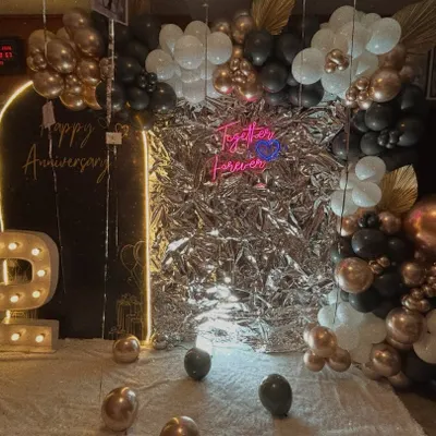 Our 'Bling Bling' decor is perfect for adding glamour to any anniversary. This setup features a stunning silver foil backdrop, a 'Happy Anniversary' neon sign, a light-up number '2', and a black, white, and rose gold balloon garland.