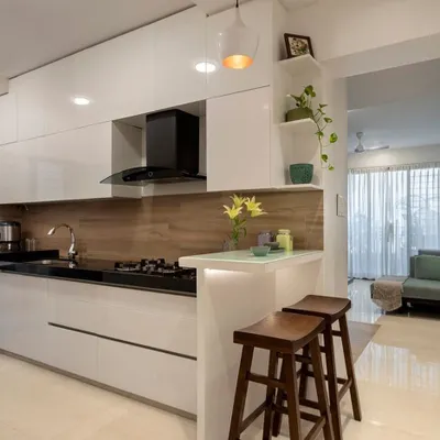 A look at a modern kitchen renovation we completed, designed for seamless cooking and entertaining. This space features handleless glossy white cabinets for a clean, minimalist look, a functional breakfast counter for casual meals, and a warm wood-textured backsplash. We focus on smart layouts that combine high-end appliances with ample storage and workspace.