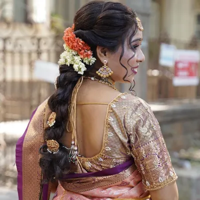 A detailed back view of a contemporary bridal braid. This style combines traditional braiding techniques with modern sensibilities, using both flowers and classic hair accessories to match the bride's Kanjivaram saree.