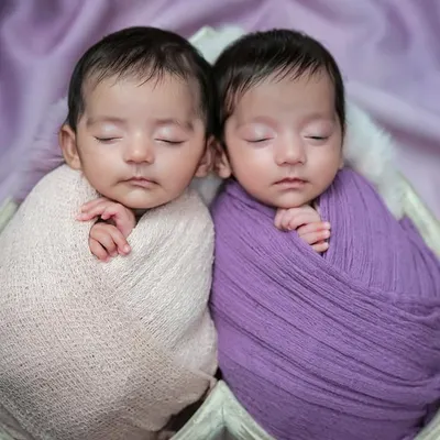 A close-up of newborn twins nestled together in a heart-shaped prop. Swaddled in complementary shades of pink and purple, this image beautifully highlights their peaceful bond.