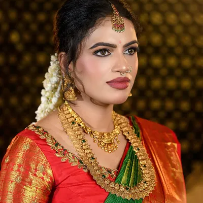 A complete look at a traditional South Indian bride in a stunning green and red Kanjivaram silk saree. The makeup features defined eyes, a bold matte lip, and a flawless base that complements the antique gold jewelry.