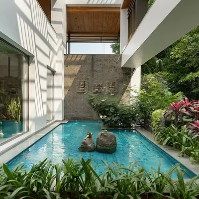 A tranquil pool nestled between the wings of a modern house, surrounded by lush tropical plants with red and green foliage. The design creates a private, resort-like escape right at home.