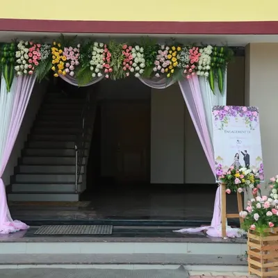 A beautiful entrance for an engagement ceremony. The arch is decorated with pastel flowers and soft pink drapes, with a welcome board and floral crates greeting the guests.