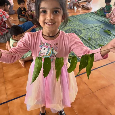 A smiling child shows off the 'thoran' she made from leaves during summer camp. Our camp activities are often inspired by nature and hands-on creativity.