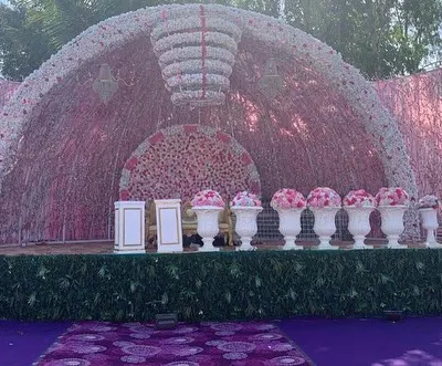 This magnificent reception stage is a showcase of floral artistry, featuring a massive semi-circular arch made of pink and white flowers. The grand scale and intricate detail make it a breathtaking centerpiece for a large wedding.