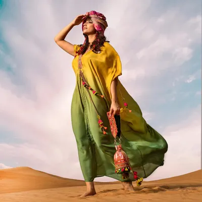 A powerful pose in the desert, with the model looking towards the horizon. The vibrant colors of the kaftan and turban stand out beautifully against the blue sky.