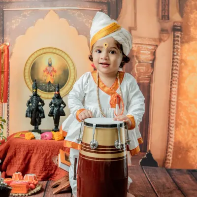 A joyful moment from a 'Chota Varkari' shoot, where the baby boy stands with a traditional pakhawaj drum. The authentic turban and attire complete this cultural portrait.