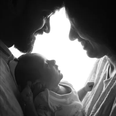 This dramatic, high-contrast silhouette captures the intimate bond between new parents and their baby. It's a powerful and artistic black and white portrait that focuses solely on their connection.