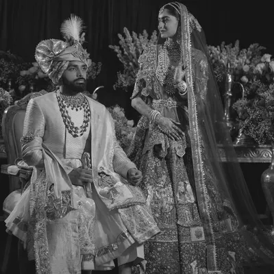 A regal portrait in monochrome. This black and white image of the couple has a timeless, classic feel, emphasizing the rich textures of their traditional attire and the gravity of the moment.