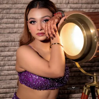 A creative studio portrait where the model leans against a vintage spotlight, creating a warm glow on her face.