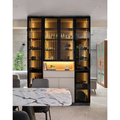 This stunning setup features a sleek, black-framed display unit with warm internal lighting, perfect for showcasing crockery and decor. The unit is paired with a beautiful marble-top dining table for a touch of class.