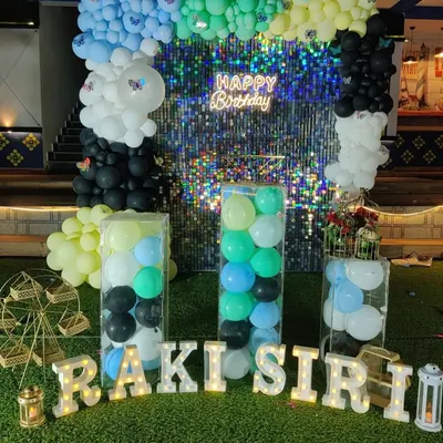 This birthday setup features a multi-colored balloon arrangement against a glittering shimmer wall. I also included light-up letters for the name and clear plinths filled with balloons for a unique touch.