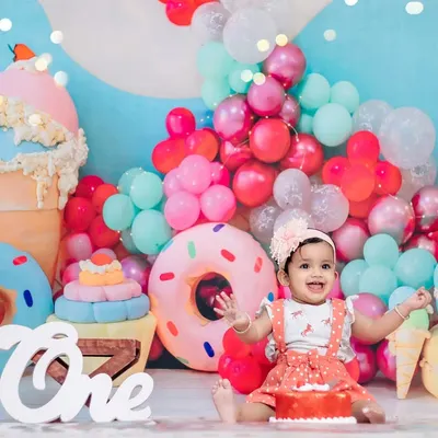 A vibrant and sweet first birthday celebration with a candy-themed backdrop, complete with giant donuts, ice cream cones, and colorful balloons. This is what pure happiness looks like.