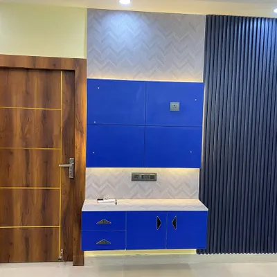 A bold and colorful entryway featuring a blue TV cabinet and a modern wooden flush door with gold inlay.