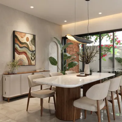 A contemporary dining space featuring a marble-top table with a fluted wooden base. The room is accented by an abstract artwork and a large plant, with glass doors opening to an outdoor area.