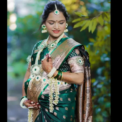 A graceful outdoor portrait of a mother-to-be, her hands gently cradling her belly. She is dressed in a traditional saree and floral jewelry for her baby shower celebration.