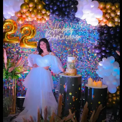 A stunning 22nd birthday celebration with a shimmering sequin backdrop. The decor is elevated with a black and gold balloon garland, foil number balloons, and custom-printed pedestals for the cake.